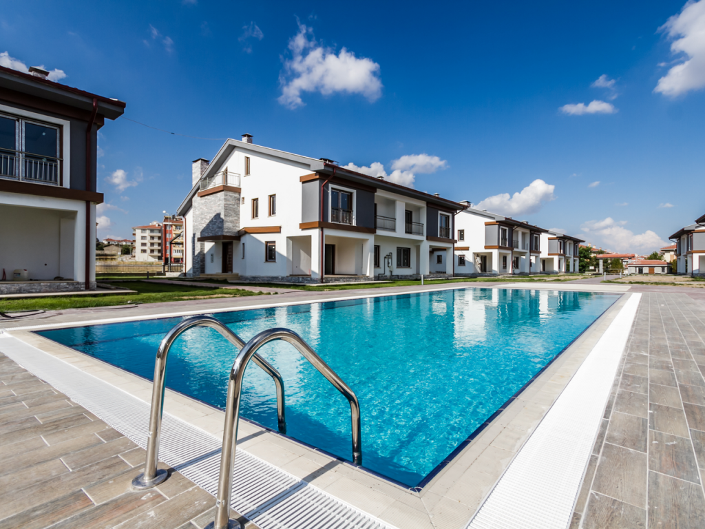 Luxury modern villas surrounding a glistening swimming pool under a clear blue sky.
